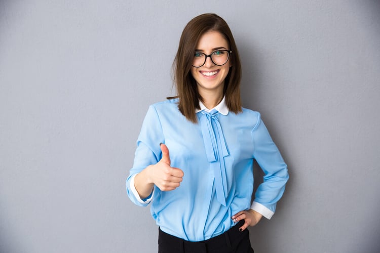 Happy businesswoman showing thumb up over gray background. Wearing in blue shirt and glasses. Looking at camera_seo-opt