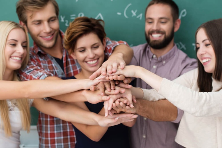 Teamwork and collaboration amongst students with a laughing group of diverse young men and women standing close together forming a stack with their hands_seo-opt-1