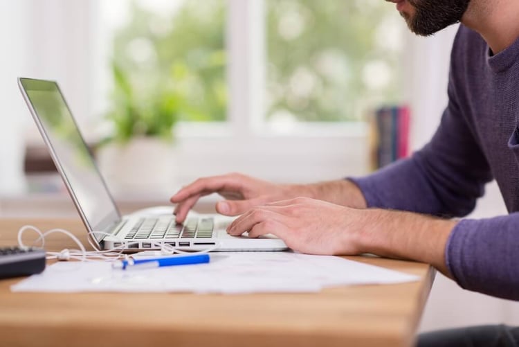 Close up low angle view of a man working from home on a laptop computer sitting at a desk surfing the internet_seo-opt