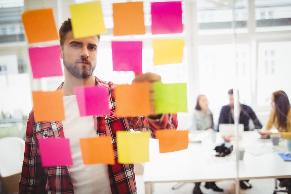 Photo editor looking at multi colored sticky notes on glass in meeting room at creative office-1