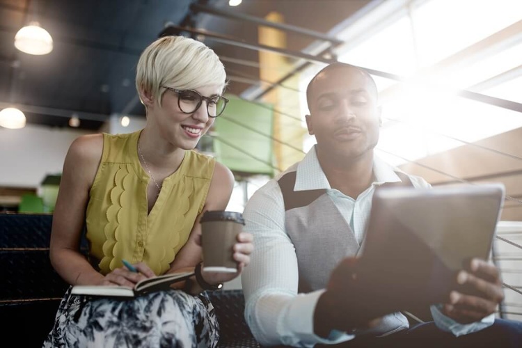 Two creative millenial small business owners working on social media strategy using a digital tablet while sitting in staircase_seo-opt-1